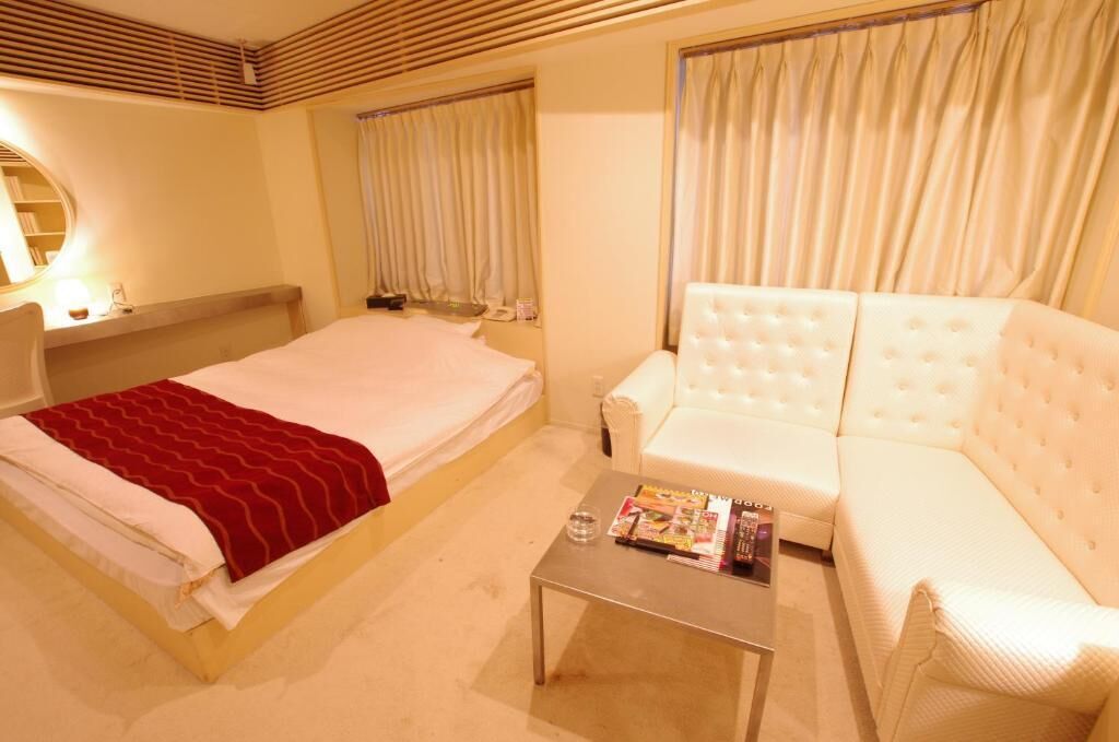 A hotel room with a bed, a white sofa, a small table, and curtains.