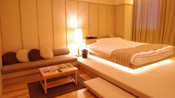 Una habitación de hotel con cama, sofá, una mesita y una lámpara.
