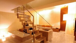 Un salón moderno con una escalera de cristal, un sofá con cojines naranja y una pared de acento de madera.