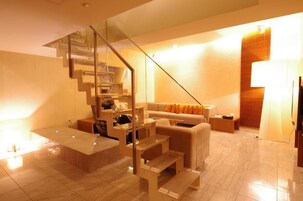 Un salon moderne avec un escalier en verre, un canapé agrémenté de coussins orange et un mur d’accent en bois.