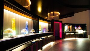 Un moderno vestíbulo de hotel con una larga barra de recepción que exhibe diferentes alimentos, iluminación ambiental y una zona de bar.