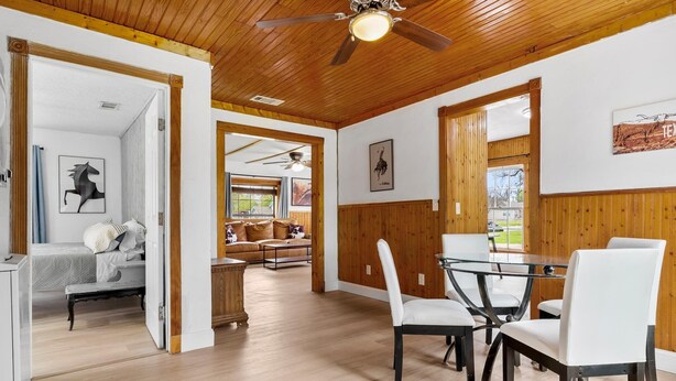 A spacious room with a wooden ceiling, a dining area with a glass table and chairs, and a cozy seating area with a sofa and a side table. - Charming Home Near Stockyards & Trinity Trails Central Fort Worth (River Oaks)