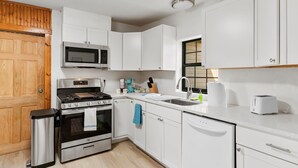A compact kitchen with white cabinets, a microwave, a stove, a sink, and a dishwasher. - Charming Home Near Stockyards & Trinity Trails Central Fort Worth (River Oaks)