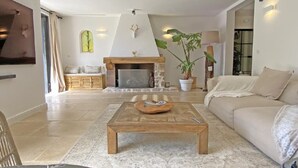 Ein Wohnzimmer mit Kamin, einer Couch, einem Couchtisch und einer großen Pflanze.