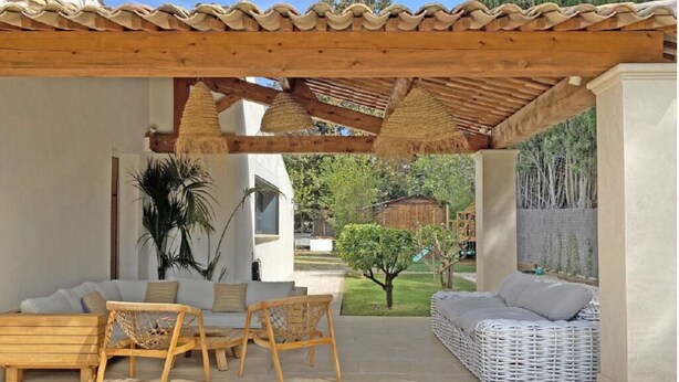 Eine Terrasse im Freien mit einer Pergola, Korbmöbeln und einem weißen Sofa.
