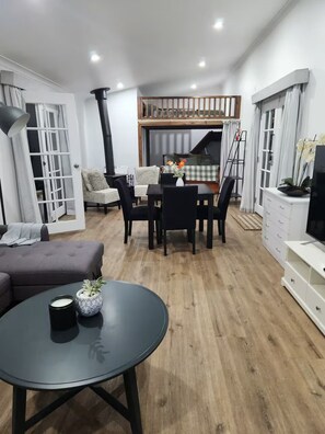 Een moderne woonkamer met een eetgedeelte, een bank, een televisie en een trap naar een verdieping.