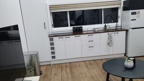 Une cuisine moderne avec des armoires blanches, un four encastré, un réfrigérateur et une fenêtre équipée de stores.