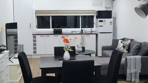 Une cuisine moderne avec des meubles blancs, une table à manger avec des chaises, un canapé gris et une grande fenêtre.