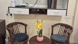 Un salon équipé d’un téléviseur à écran plat, d’une machine à café, d’un vase avec des fleurs, de deux fauteuils et d’une petite table.