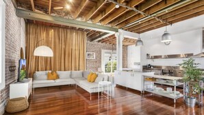A modern kitchen with white cabinets and stainless steel appliances, a wooden ceiling, and a dining area with a white table and chairs. - New York-Style Loft in Sydney CBD (Darlinghurst)