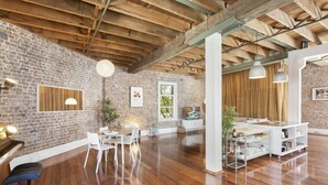 A spacious room with exposed brick walls, wooden beams, a piano, white furniture, and pendant lighting. - New York-Style Loft in Sydney CBD (Darlinghurst)