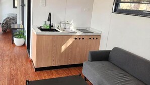 Ein kompakter Wohnbereich mit Küchenzeile, einem grauen Sofa, einem schwarzen Couchtisch und einem Fenster.