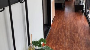 Ein Flur mit Holzboden, einem Bett im Hintergrund und einer Pflanze auf dem Boden.