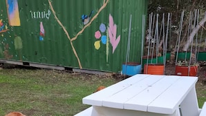 Dos perros sentados sobre césped cerca de una mesa de picnic blanca.
