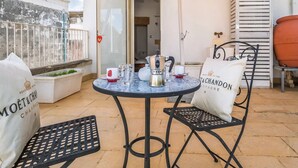 Eine Terrasse mit einem runden Tisch, zwei Stühlen, einem gelben Sonnenschirm und einer weißen Tasche mit Schrift.