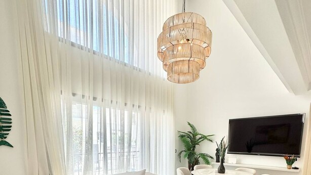 Een moderne woonkamer met een hoekbank, een ronde salontafel, een opvallende groene fauteuil, een grote televisie en een hanglamp.