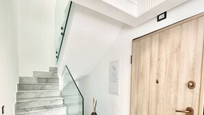 Een marmeren trap die leidt naar een plateau met een glazen balustrade, een houten deur en een kleine vaas op een voetstuk.