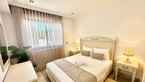Een hotelkamer met een bed, nachtkastjes, een bureau en een groot raam met gordijnen.