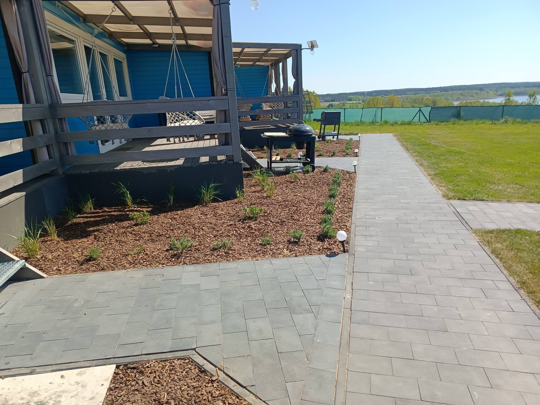 Et overdækket udendørs område med træterrasse, grill og belagt sti.