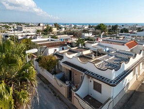 A residential area with white buildings, some with flat roofs and others with sloped roofs, surrounded by greenery and a clear sky. - Brezza Salentina House – Giardino Privato (Torre Lapillo)