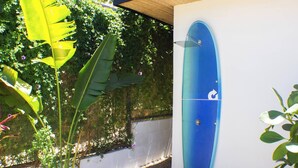 Une planche de surf bleue est fixée au mur, entourée de verdure et adossée à un mur blanc.