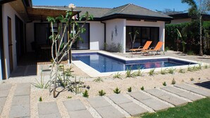 Une maison avec une piscine, deux chaises longues et un petit jardin.