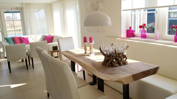 A modern living room with a dining area, white furniture, a large window with pink flowers, and a unique wooden table centerpiece. - Alkmaar Cozy Dutch Villa (West-Graftdijk)