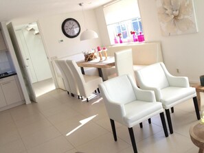 A modern living room with white furniture, a dining area with a wooden table, and a large window with pink vases. - Alkmaar Cozy Dutch Villa (West-Graftdijk)