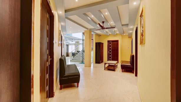 A spacious hallway with a ceiling fan, a staircase, and a seating area with a bench and two chairs. - Hotel Jacs Inn (Guwahati)