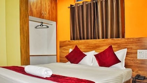 A hotel room with a bed, a wooden headboard, a red throw blanket, and a telephone on a wooden nightstand. - Hotel Jacs Inn (Guwahati)