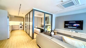 Ein modernes Hotelzimmer mit Küchenzeile, einer Couch, einem Fernseher und einer Schiebetür zu einem Badezimmer.