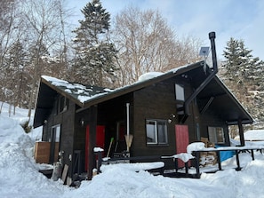 A wooden cabin with a sloped roof, a chimney, and a porch area.