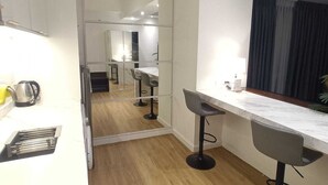 A modern kitchen with a wooden floor, white cabinets, and a large mirror. There are two bar stools and a countertop with a kettle. - Deluxe studio at AVANT in BGC (Taguig)