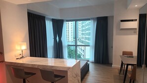 A modern kitchen with a marble island, bar stools, and a view of high-rise buildings through large windows. - Deluxe studio at AVANT in BGC (Taguig)