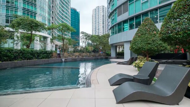 A modern outdoor pool area with lounge chairs, a water feature, and surrounding greenery. - Deluxe studio at AVANT in BGC (Taguig)
