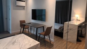 A modern hotel room with a TV, a desk, two chairs, a bed, a mirror, and a bedside lamp. - Deluxe studio at AVANT in BGC (Taguig)