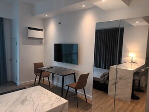 A modern hotel room with a TV, a desk, two chairs, a bed, a mirror, and a bedside lamp. - Deluxe studio at AVANT in BGC (Taguig)