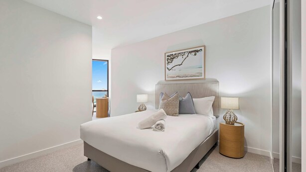 Habitación de hotel con una cama grande, dos mesitas de noche con lámparas, un cuadro en la pared y vista al mar a través de una ventana.