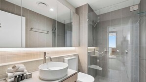 Un baño moderno con un lavamanos redondo, un inodoro y una zona de ducha con mampara de vidrio.