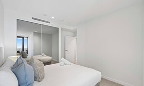 Une chambre d’hôtel moderne avec un grand lit, un miroir et une vue sur le ciel.