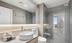 Ein modernes Badezimmer mit einem runden Waschbecken, einer Toilette, einer Duschkabine aus Glas und einem großen Spiegel.