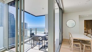 En moderne lejlighed med balkon med havudsigt, spiseområde med rundt spejl og udsigt til høje bygninger.