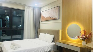 Habitación de hotel con cama, mesita de noche con espejo, una obra de arte en la pared y vistas a través de una ventana con cortinas.