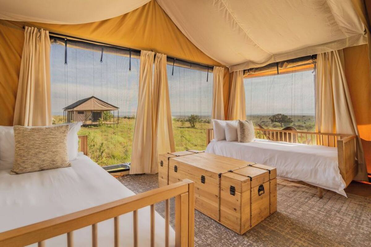 A tented room with two beds, a wooden chest, and a view of the savannah.