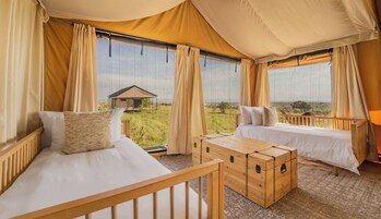 Quarto coberto por uma tenda, com duas camas, um baú de madeira e vista para a savana.