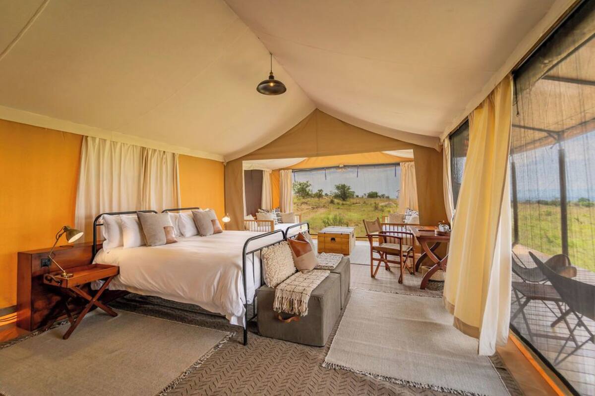 A bedroom with a bed, bedside table, lamp, and a view of the outdoors.