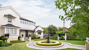A two-story house with a well-maintained garden, a fountain, and a checkered pathway.
