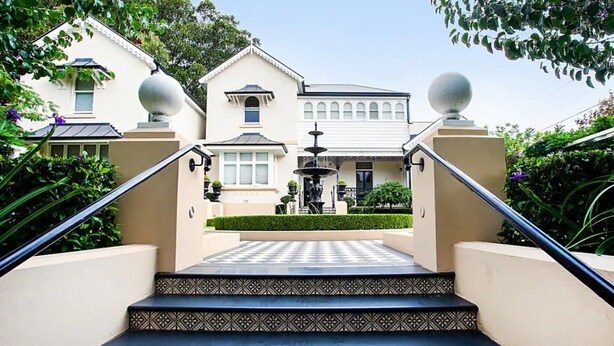 A staircase leading to a house with a fountain, surrounded by greenery.