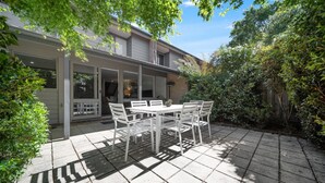 A patio with a table and chairs, surrounded by greenery and a house. - Gorgeous 2-Bed Townhouse with Patio, BBQ & Parking (Kingston)