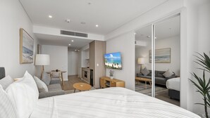 Una habitación de hotel moderna con una cama grande, un escritorio, un sofá, un televisor y una zona de comedor.